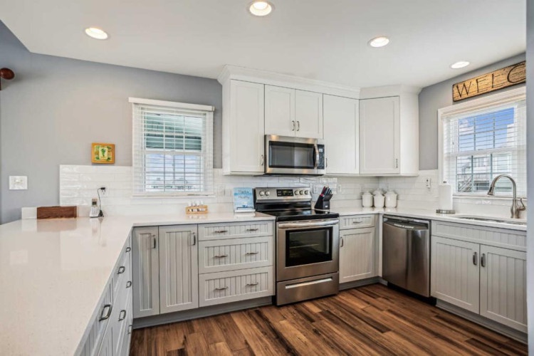 Picture yourself preparing meals in this bright, fully-equipped kitchen with modern stainless appliances, gleaming countertops, and charming coastal-inspired cabinetry—your home away from home awaits.
