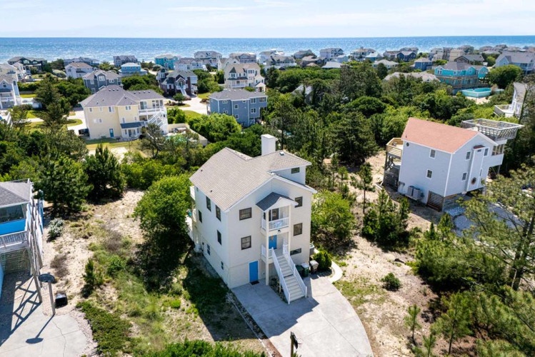Elevated view of a coastal community showcasing the property's peaceful location near sandy shores, surrounded by mature trees and neighboring beach homes.