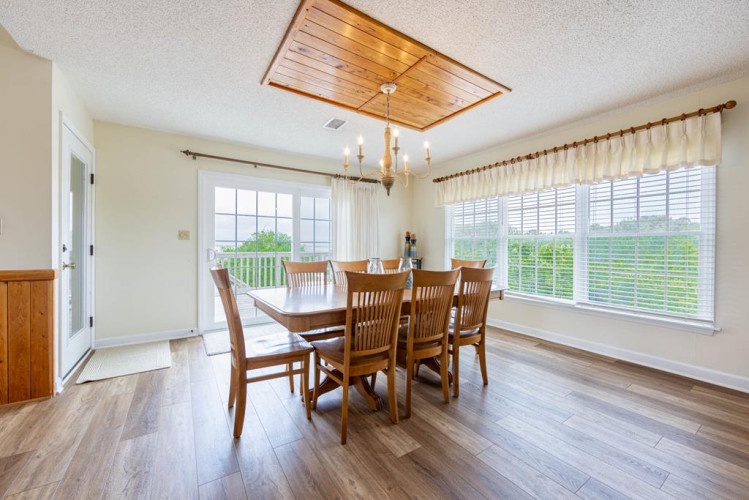 A sun-filled dining space invites you to share memorable meals around a handsome wood table, with natural light streaming through large windows overlooking lush greenery and direct access to your private outdoor retreat.