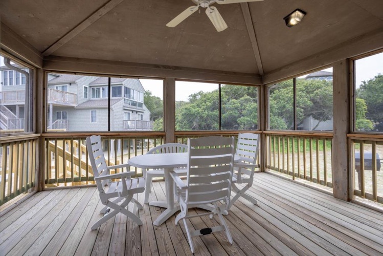 Sip your morning coffee in this screened porch, where coastal breezes drift through as you gaze out at lush greenery and neighboring beach homes—your peaceful spot between adventures.