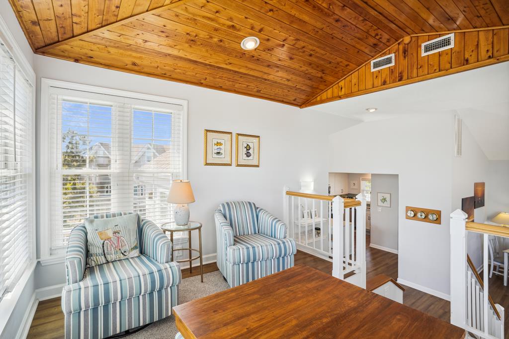 You'll love the cozy charm of this seating area with its vaulted wood ceiling, striped coastal chairs, and warm natural light streaming through the windows, perfect for relaxing.