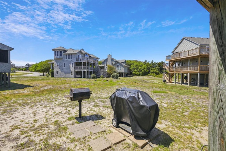 Vacation homes sit near a grassy common area, offering a peaceful coastal setting. A grill and mailbox anchor the shared outdoor space.