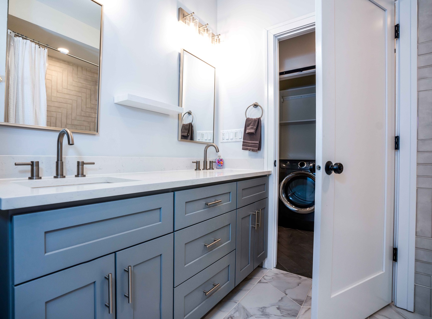 This sleek full bath features a double vanity, shower/tub combo, & laundry