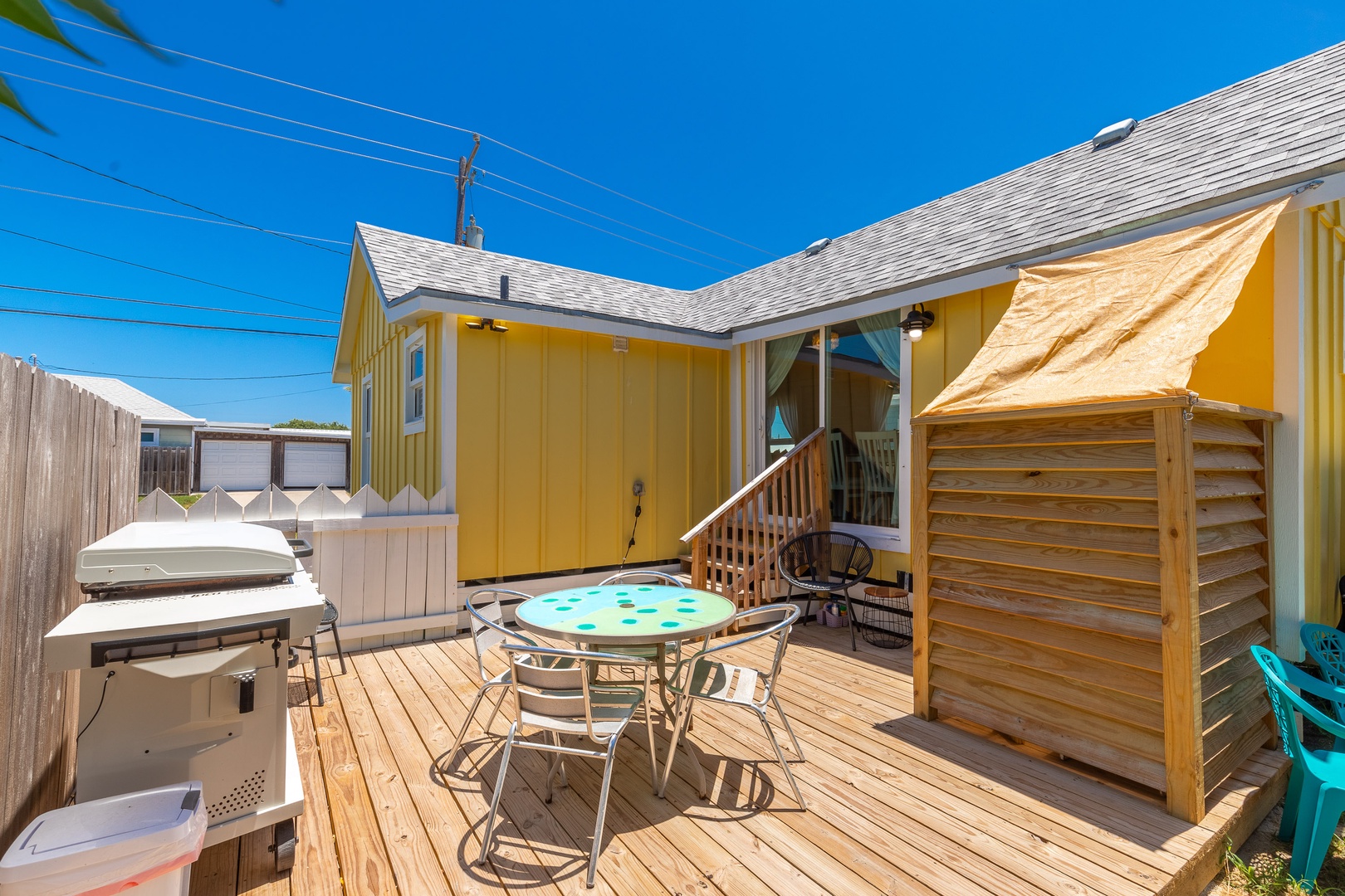 The sunny back deck is outfitted with an outdoor shower, dining set, & grill