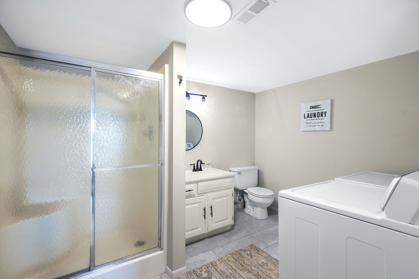 This lower-level full bath includes a single vanity, shower, & private laundry