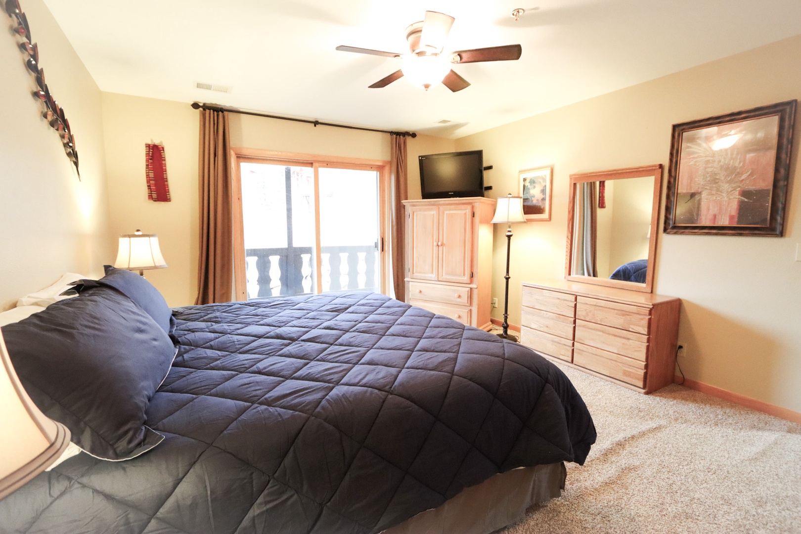 The large king bedroom includes a TV, ceiling fan, & balcony access