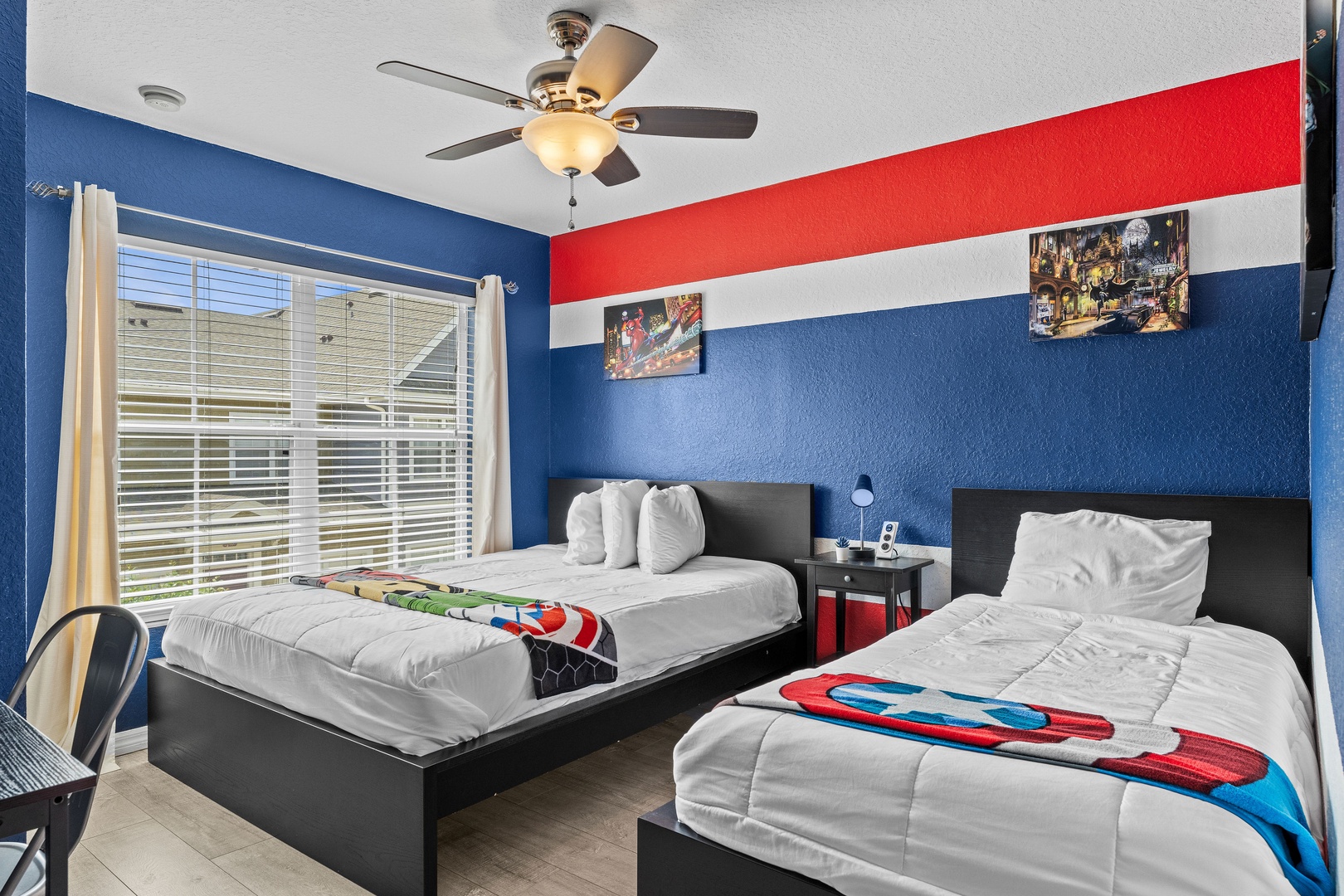 Marvel-themed bedroom with a twin and full bed, ceiling fan, and dedicated desk space