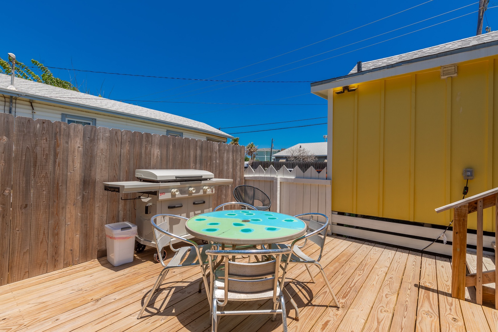 The sunny back deck is outfitted with an outdoor shower, dining set, & grill