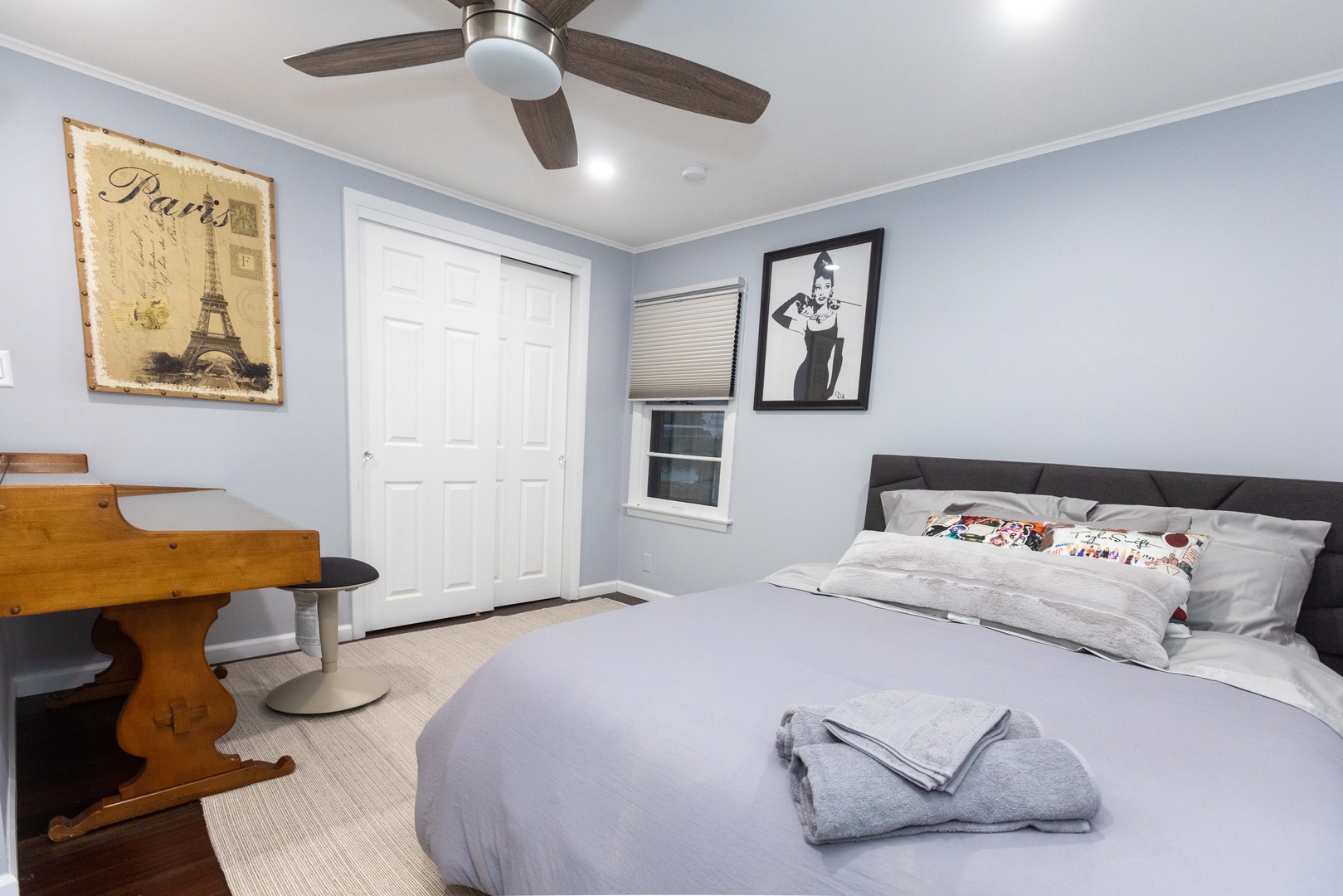 The bedroom includes a full-sized bed, desk workspace, & ceiling fan