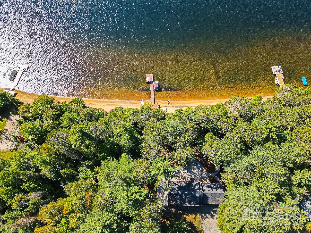 Aerial view showcases the property's stunning lakefront location, surrounded by lush forest with private beach access and dock facilities.