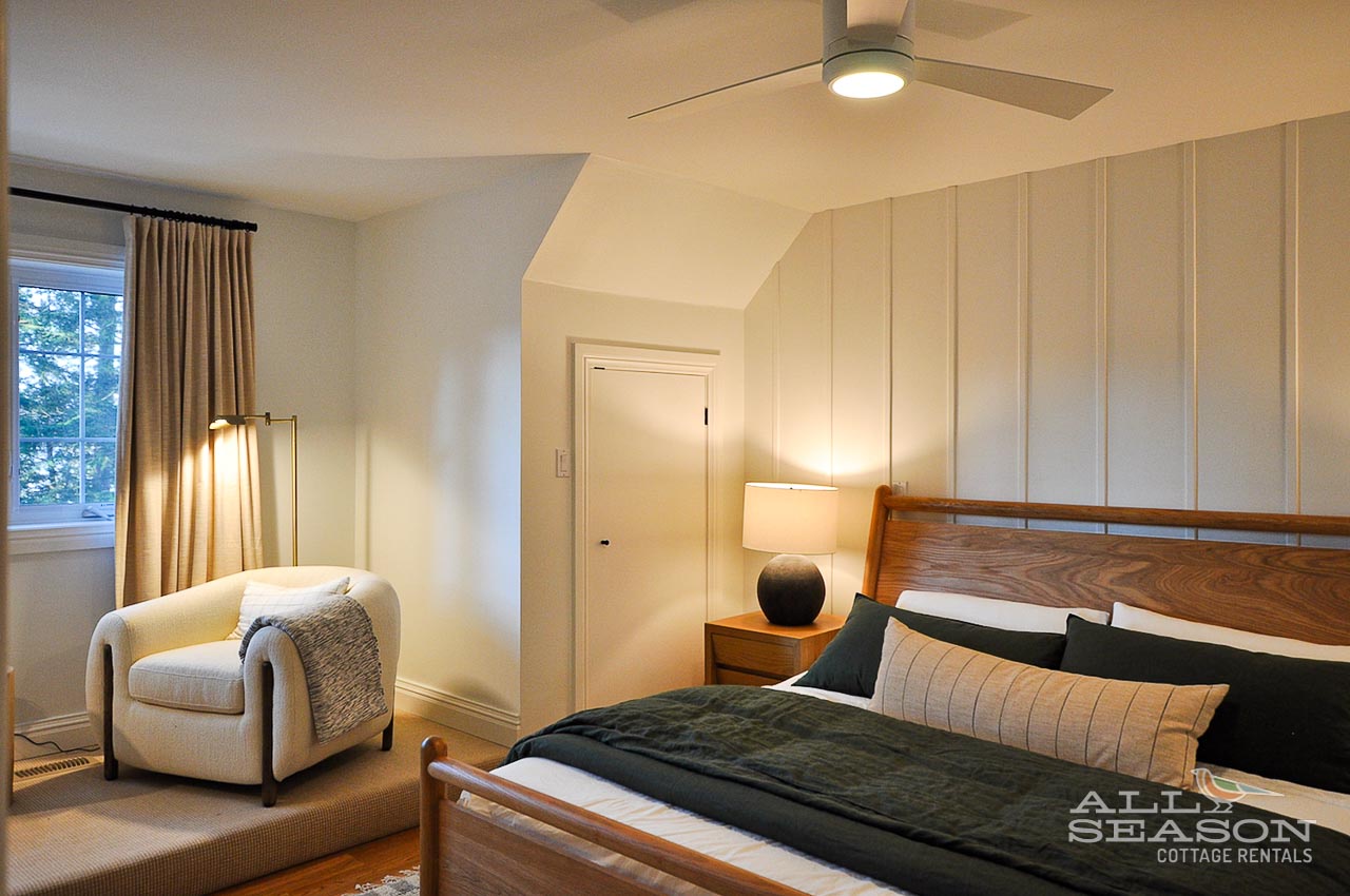 Unwind in your serene bedroom with crisp linens, cozy reading chair, and warm ambient lighting from the ceiling fan overhead.