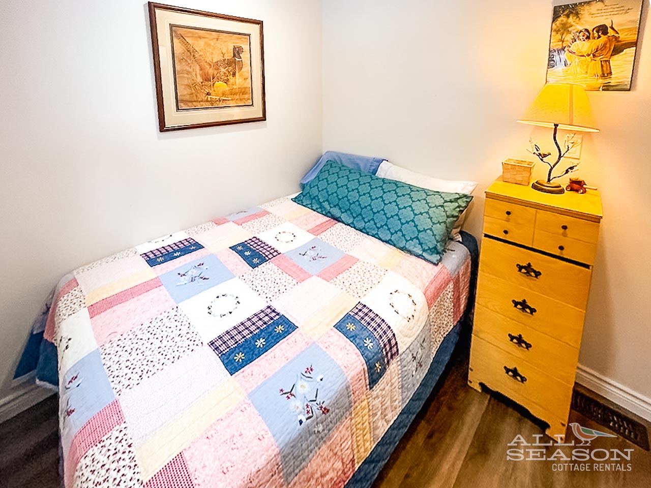 Rest peacefully in your cozy bedroom with charming patchwork bedding and warm yellow accents creating the perfect cottage atmosphere.