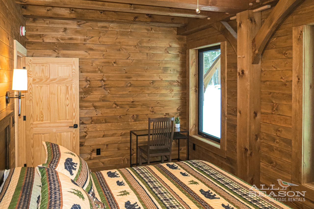 Cozy cabin bedroom with rustic wood walls, charming reading nook, and peaceful winter views from your window.