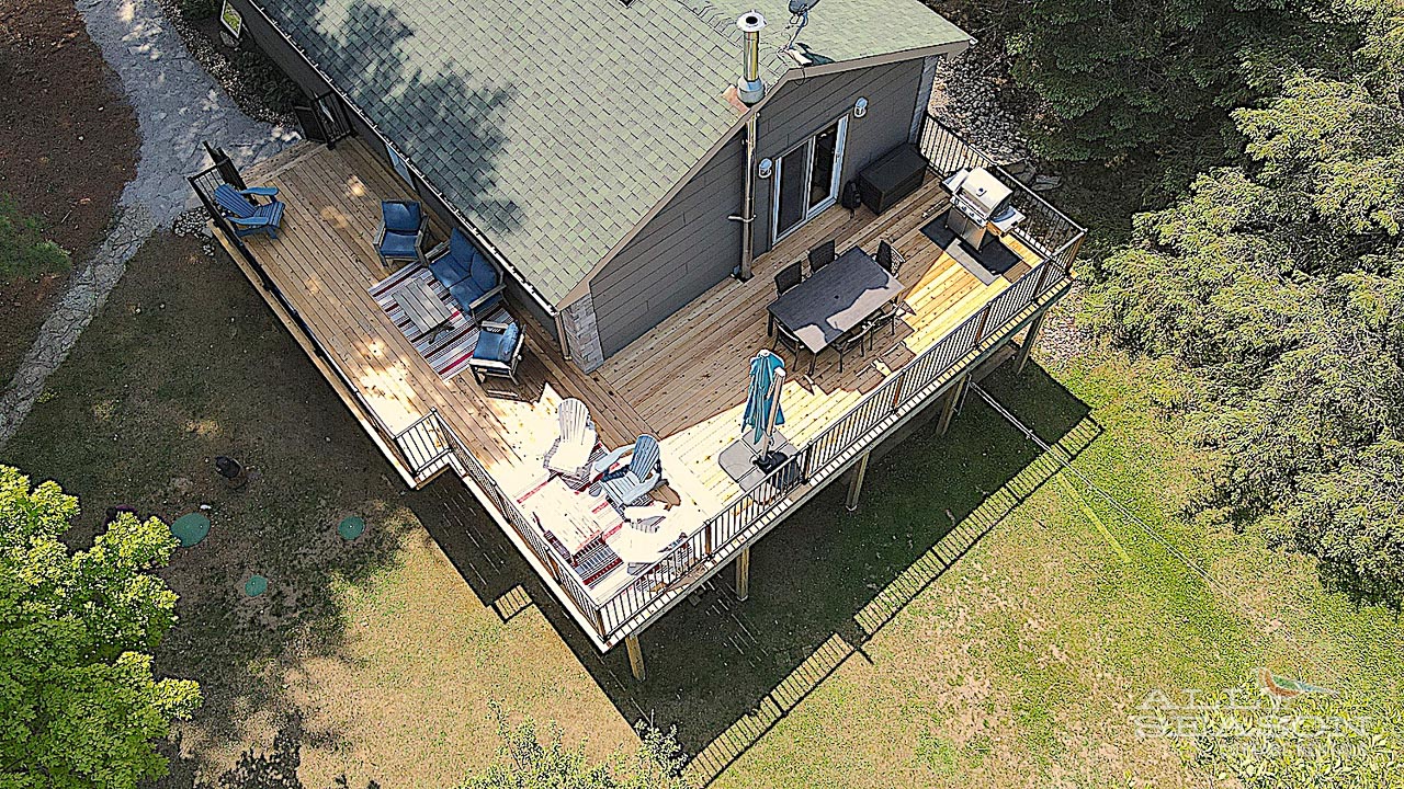 Aerial view of waterfront vacation home with expansive multi-level deck featuring outdoor dining and lounging areas on peaceful lakeside setting.