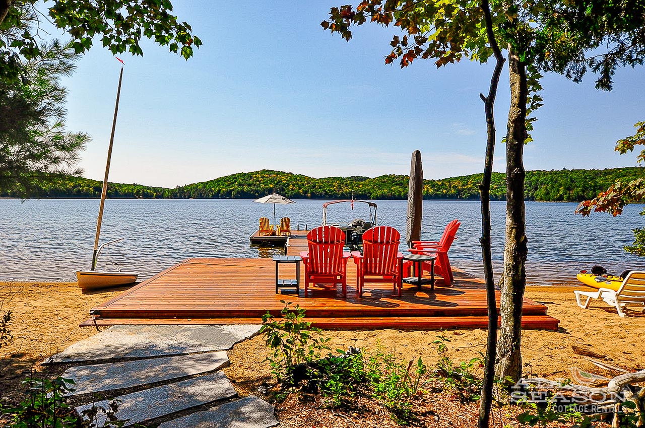 Waterfront dock with Adirondack chairs overlooking serene lake surrounded by forested hills.