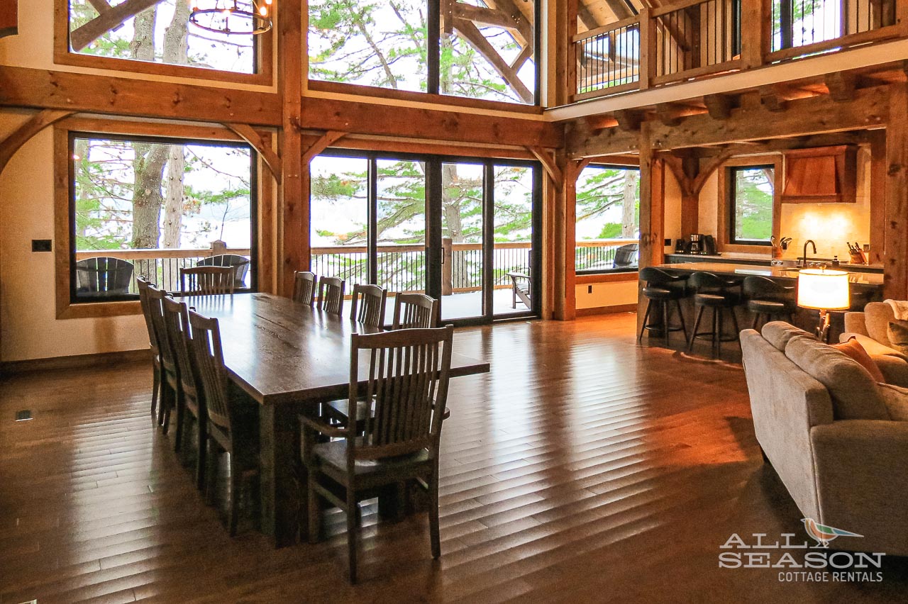 Step into your rustic retreat where natural wood beams frame lakefront views through floor-to-ceiling windows, creating perfect moments for shared meals and quiet relaxation.