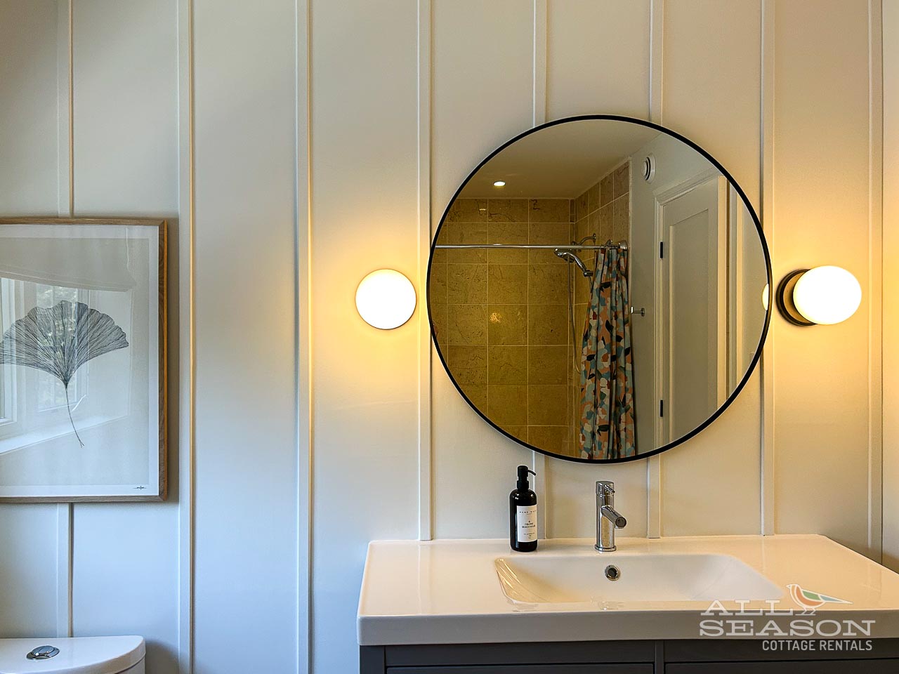 Your bright, modern bathroom features a large round mirror, warm ambient lighting, and a stylish tiled shower—perfect for refreshing after your adventures.