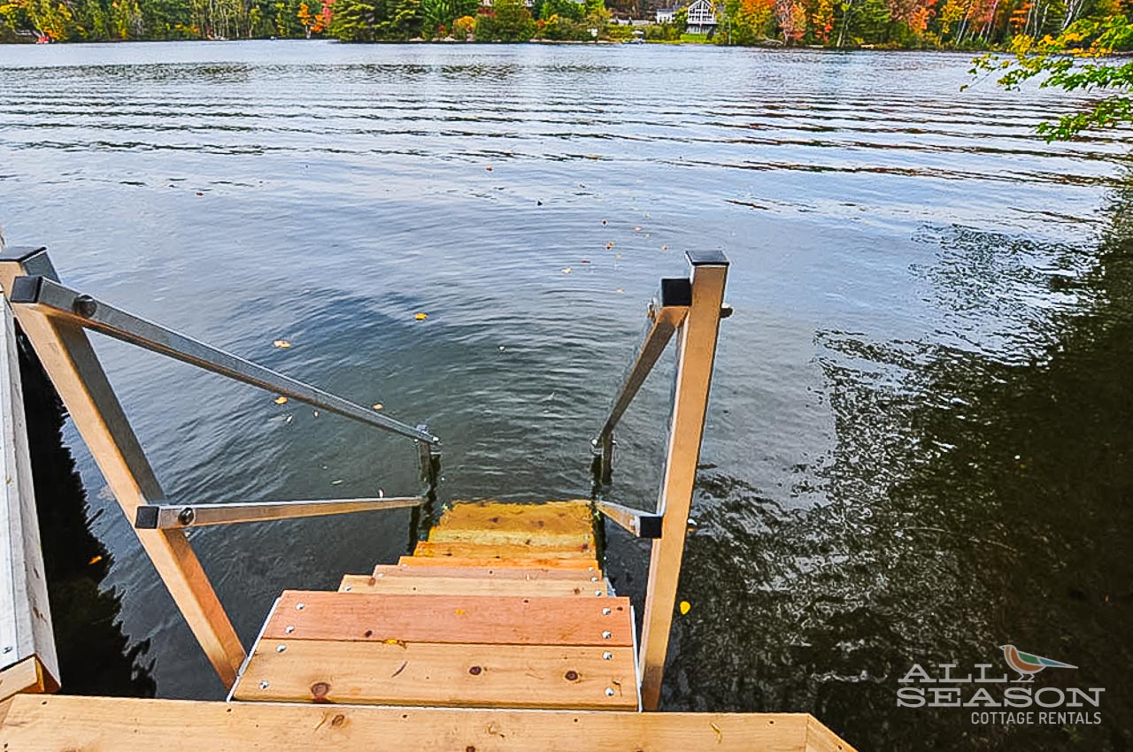 Step into crystal-clear lake waters from your private dock, surrounded by vibrant autumn foliage reflecting in the calm surface.