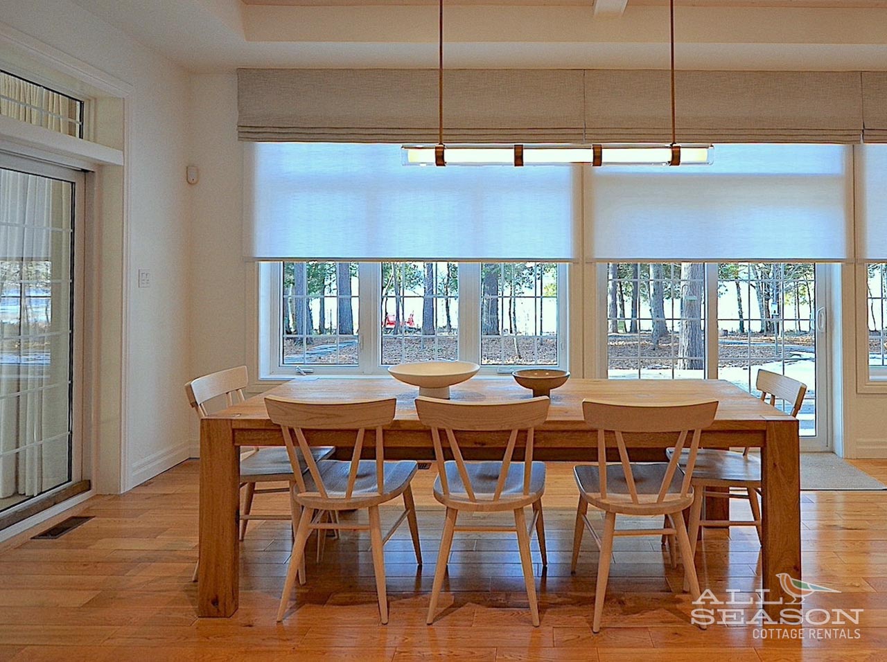 Gather around this beautiful wooden dining table where natural light streams through large windows, creating the perfect spot for memorable meals together.