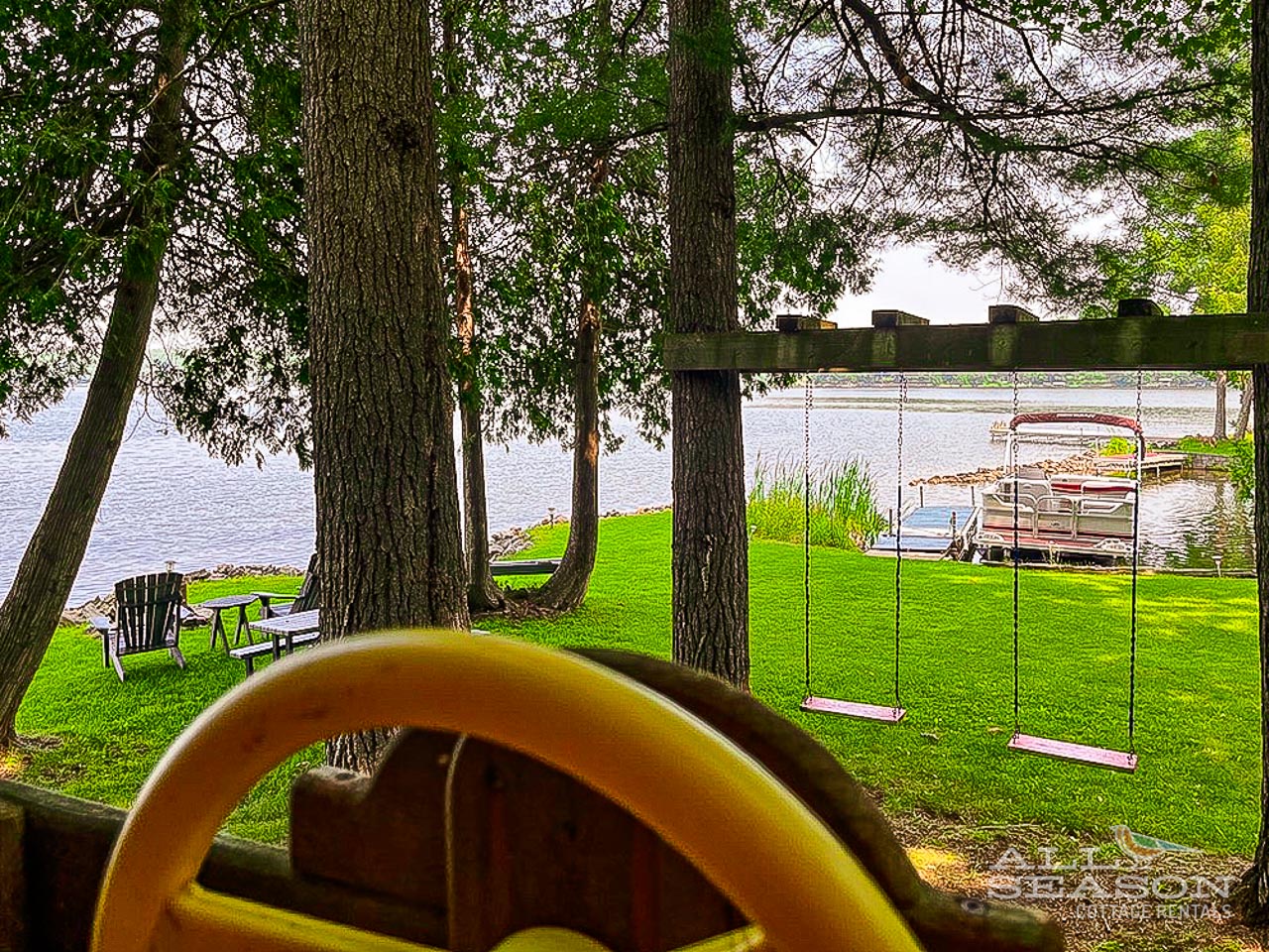 Lakefront property featuring a waterfront lawn with mature trees, swing set, dock, and pontoon boat access for memorable family vacations.