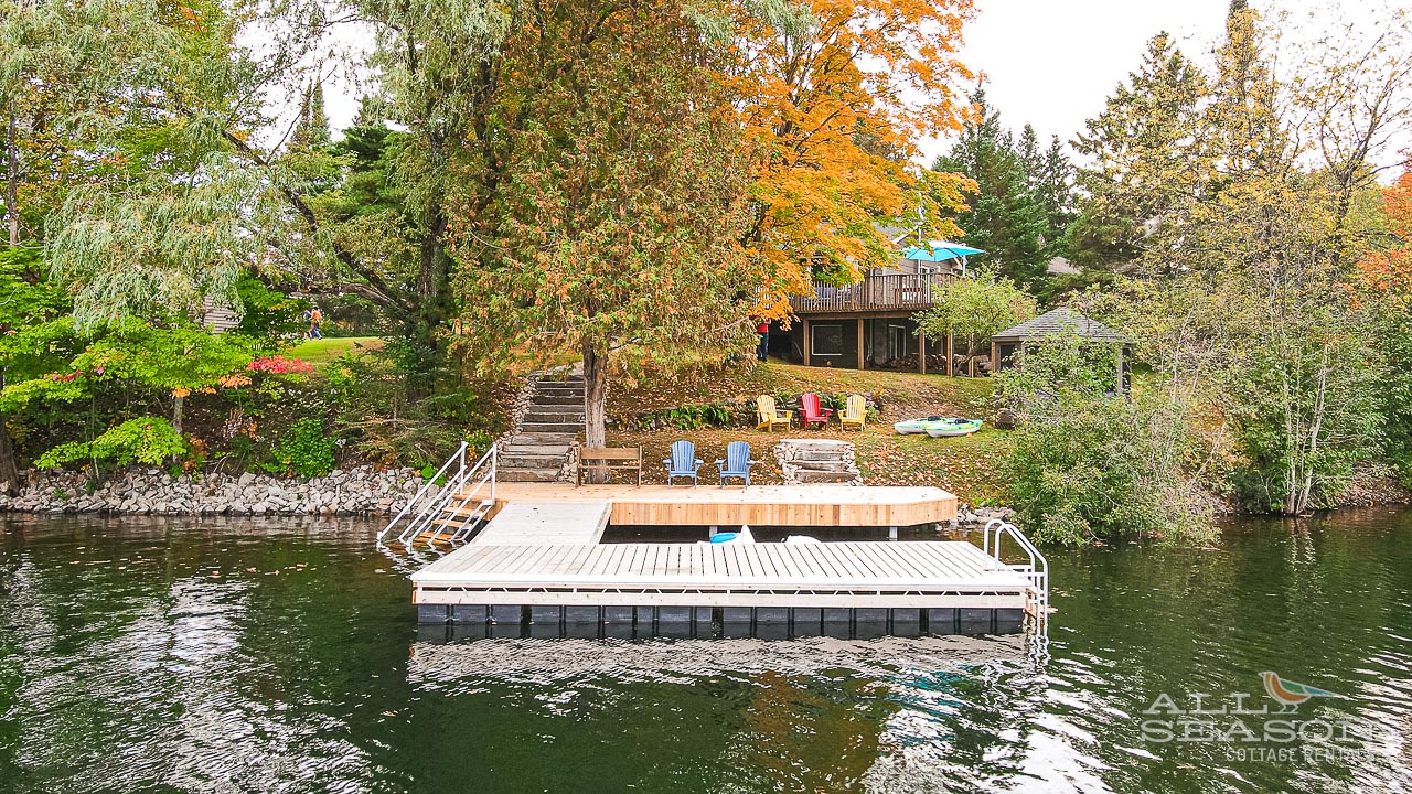 Beautiful lakefront property with private dock surrounded by vibrant autumn foliage and mature trees.