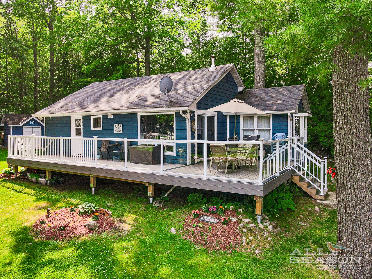 Charming lakeside cottage surrounded by towering trees and landscaped gardens in a peaceful woodland setting.