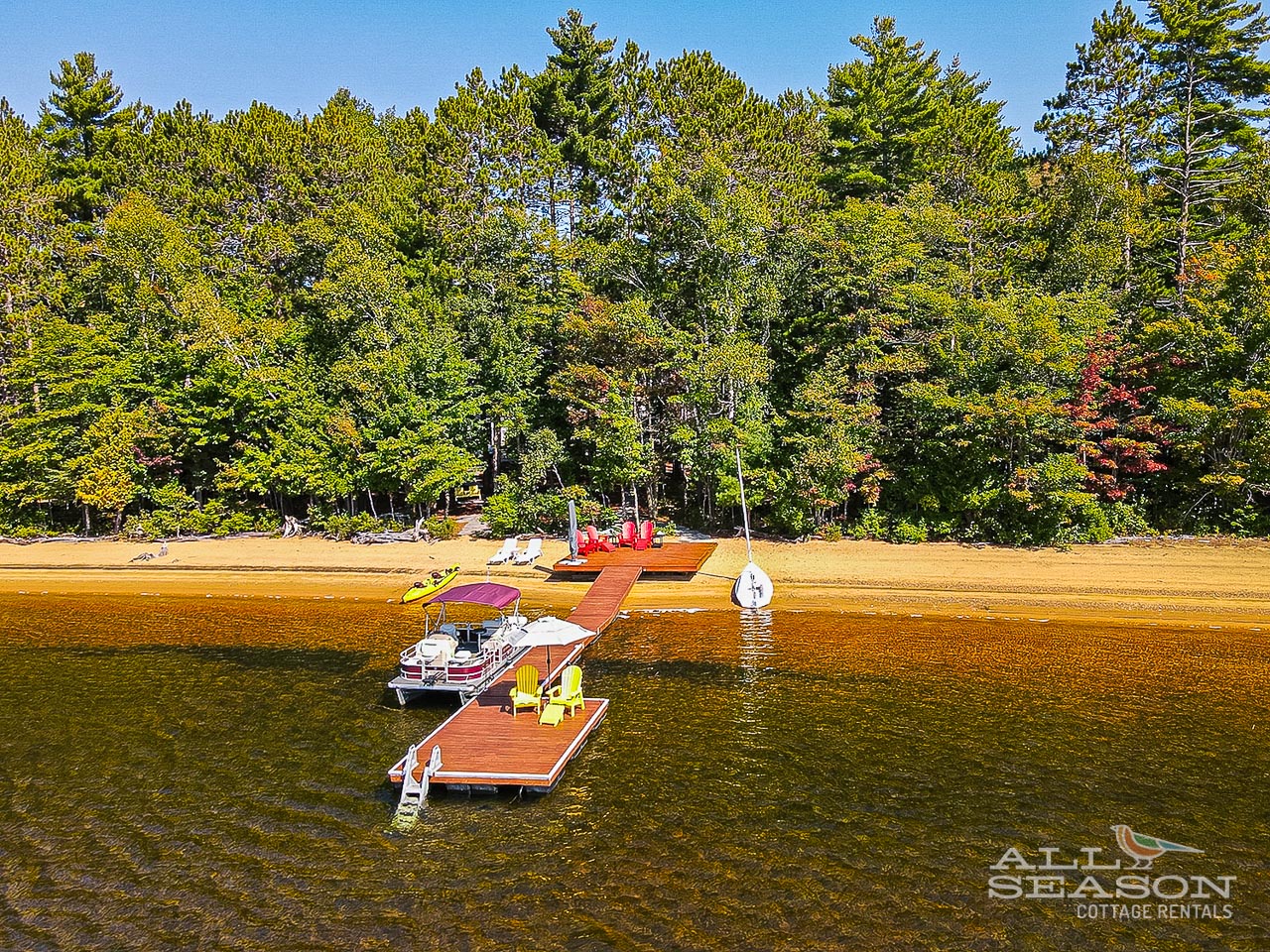 Pristine lakefront with private dock, sandy beach, and lush forest backdrop creates the perfect waterfront escape.