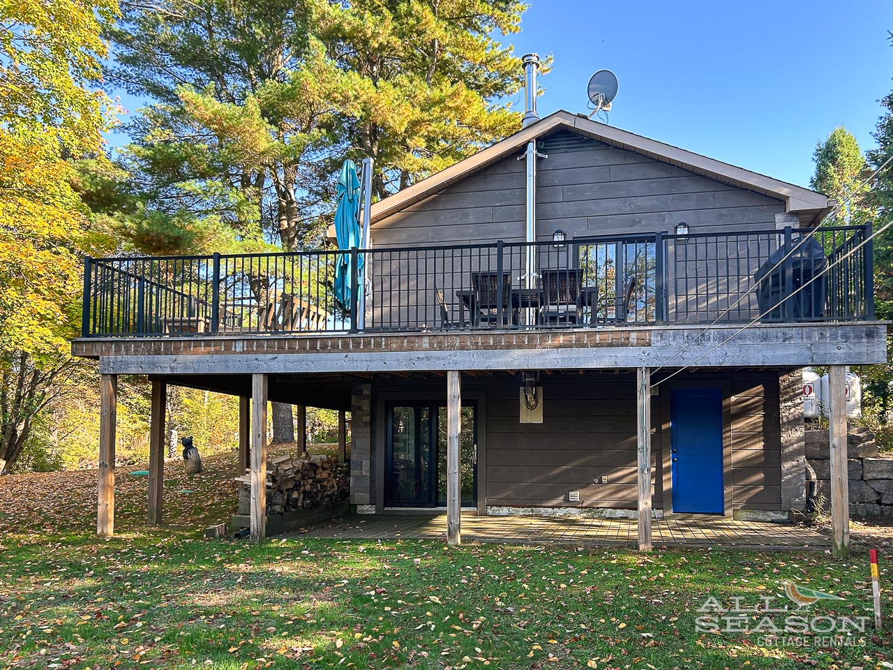 Modern lakeside cottage with spacious deck surrounded by vibrant autumn trees and peaceful natural setting.