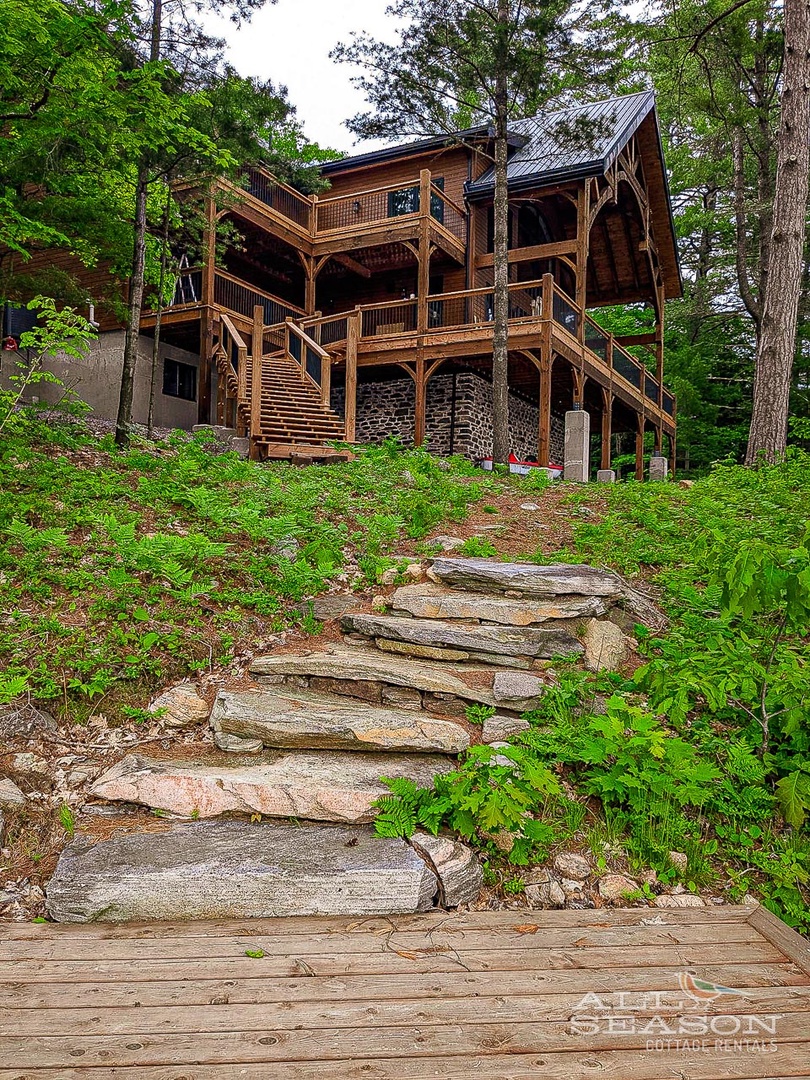 Natural stone steps lead to this stunning lakeside retreat nestled among towering pines and lush forest greenery.