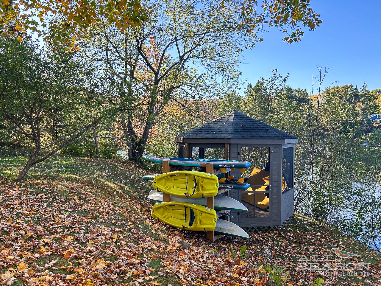 A waterside equipment shed stocked with colorful kayaks and canoes awaits your next lakeside adventure amid beautiful autumn foliage.