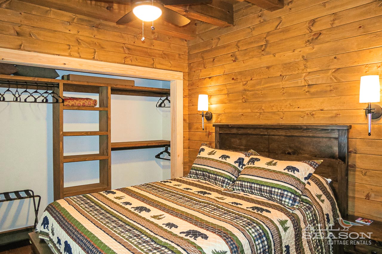 Your rustic cabin bedroom features warm wood walls, cozy bear-themed bedding, and thoughtful lighting for peaceful mountain retreat nights.