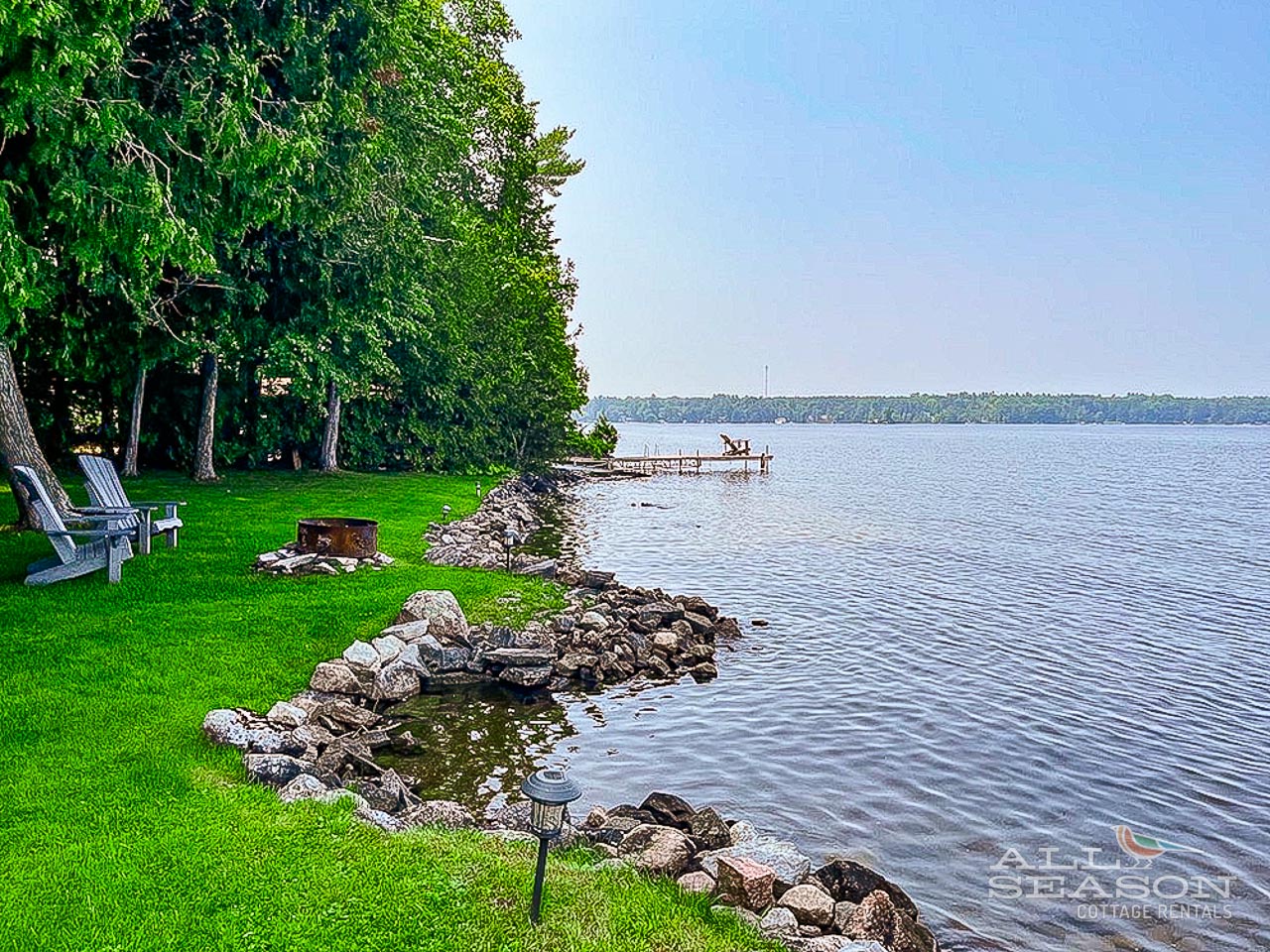 Waterfront property featuring pristine lake access with private dock and manicured lawn extending to rocky shoreline.