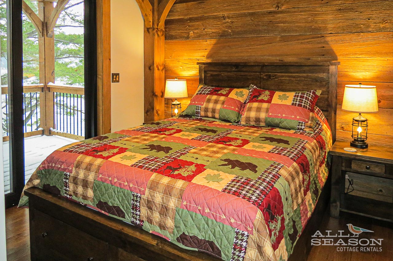 Snuggle into your cozy log cabin bedroom with rustic charm, warm lighting, and peaceful forest views from your private balcony.