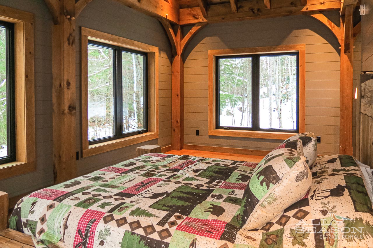 Wake up to stunning forest views through your rustic bedroom's windows, surrounded by warm timber beams and cozy quilts.