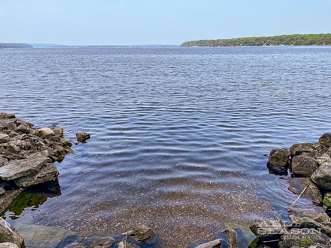 Serene lake waters stretch toward forested shores, creating a peaceful natural setting near the property.