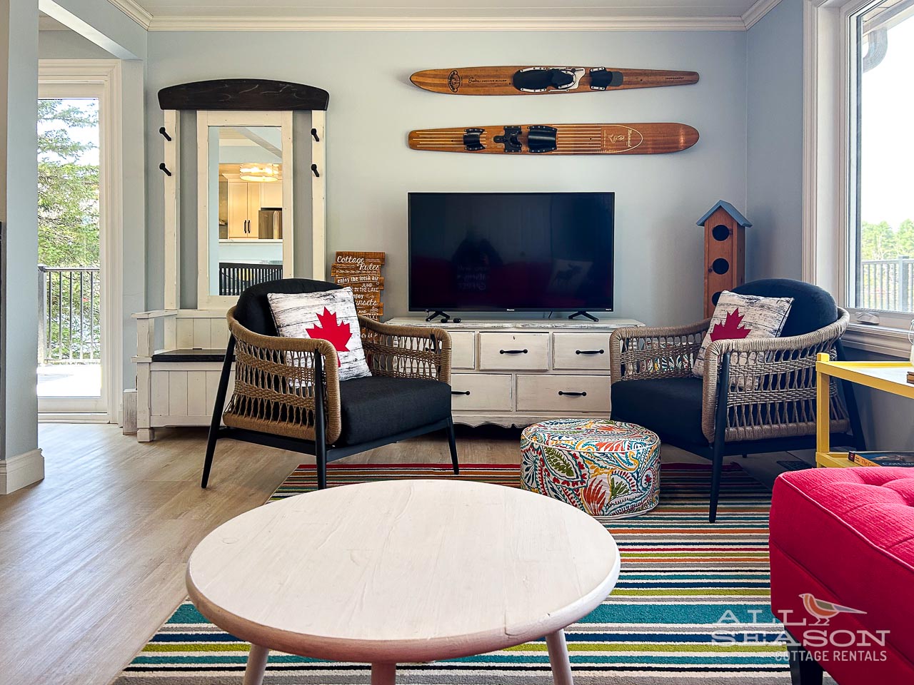 Relax in your cozy living room featuring vintage water skis, wicker chairs with Canadian flair, and a large TV for movie nights together.