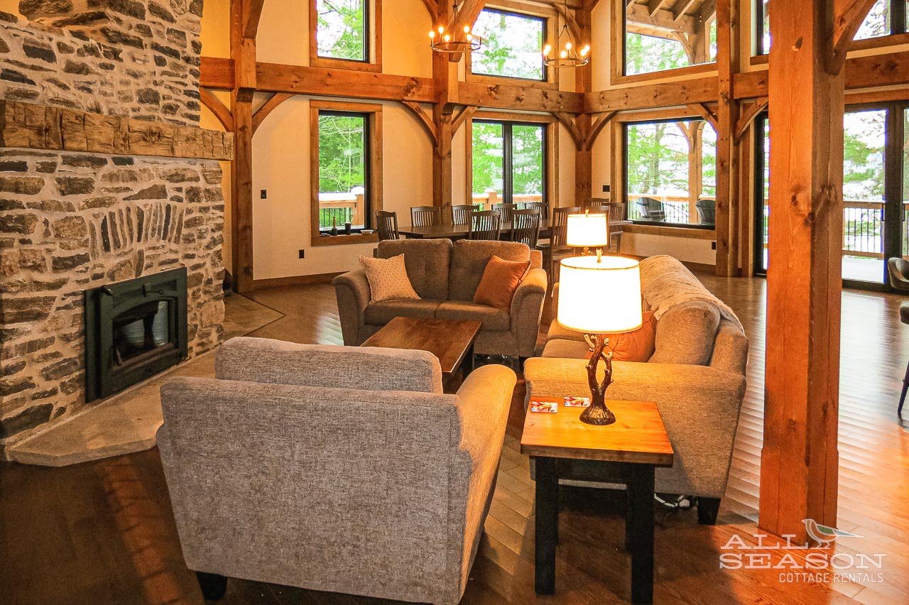 Sink into plush seating beside the stone fireplace, where timber beams frame mountain views through soaring windows in this inviting great room.