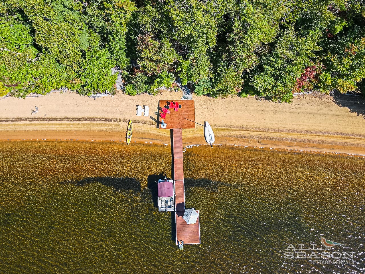 Aerial view showcases the property's stunning lakefront location with private dock and pristine sandy beach, surrounded by lush forest.