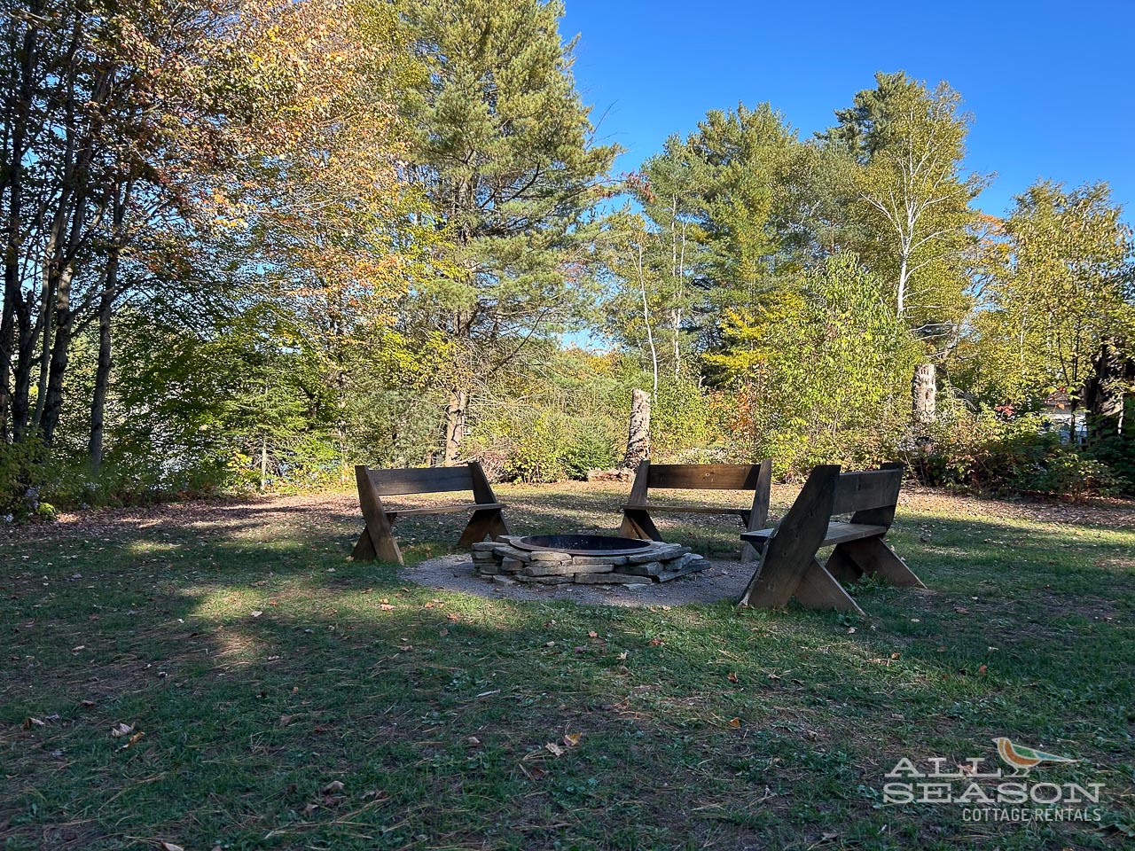 Cozy fire pit surrounded by comfortable wooden chairs where you can gather for evening conversations under the autumn canopy.