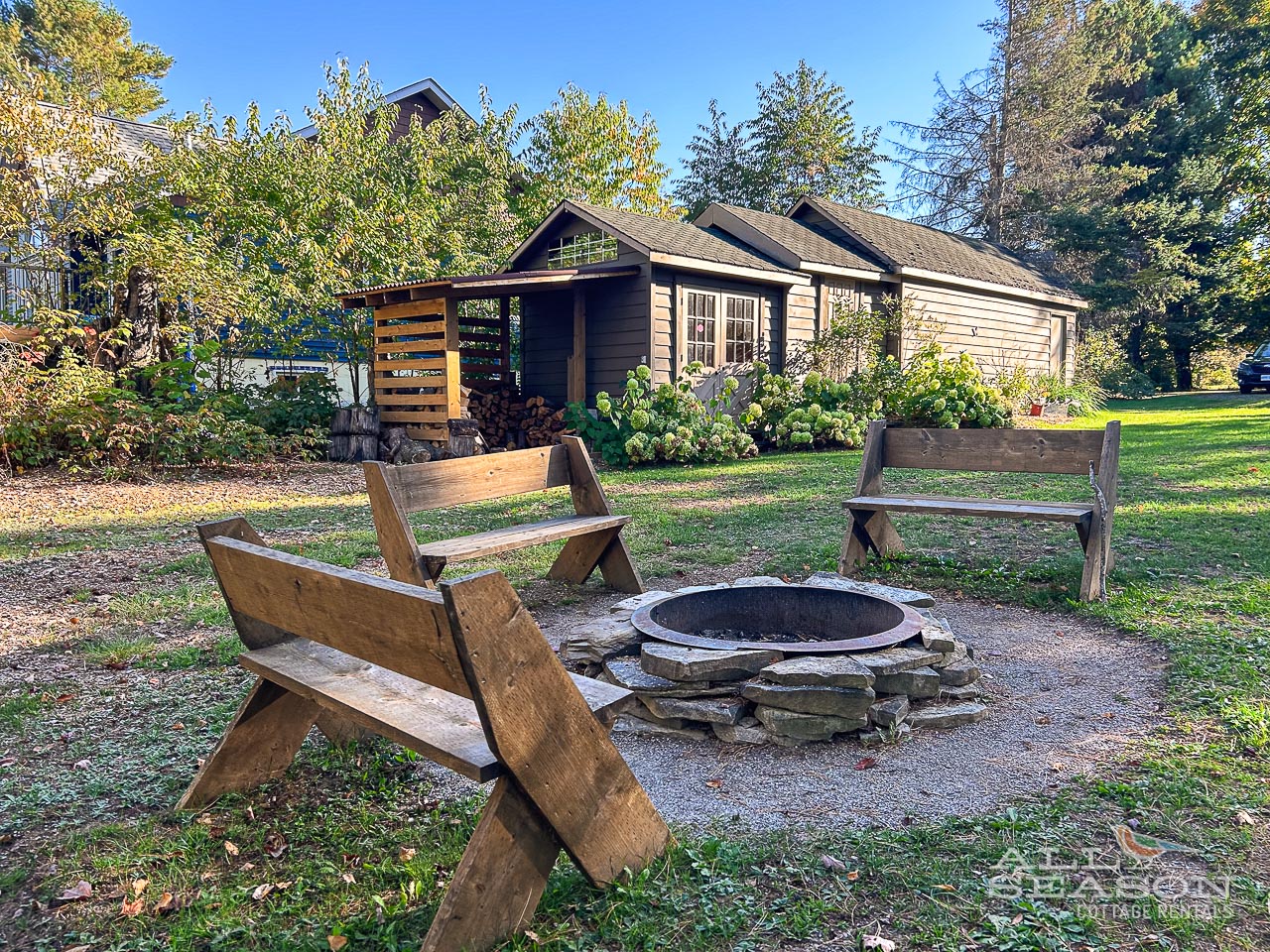 Gather around the stone fire pit on cozy wooden benches, surrounded by lush gardens and towering trees.