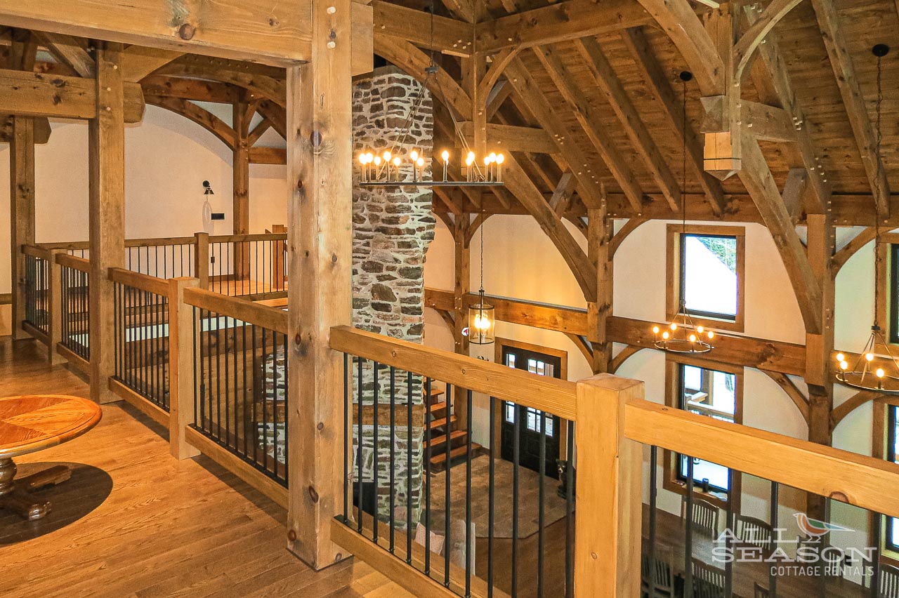 Admire the stunning timber-frame architecture from this upper loft, where exposed beams and stone fireplace create rustic elegance throughout your mountain retreat.