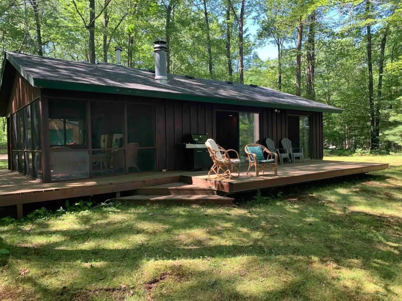 A charming forest cabin surrounded by towering trees, featuring a welcoming wooden deck with seating and peaceful woodland views.