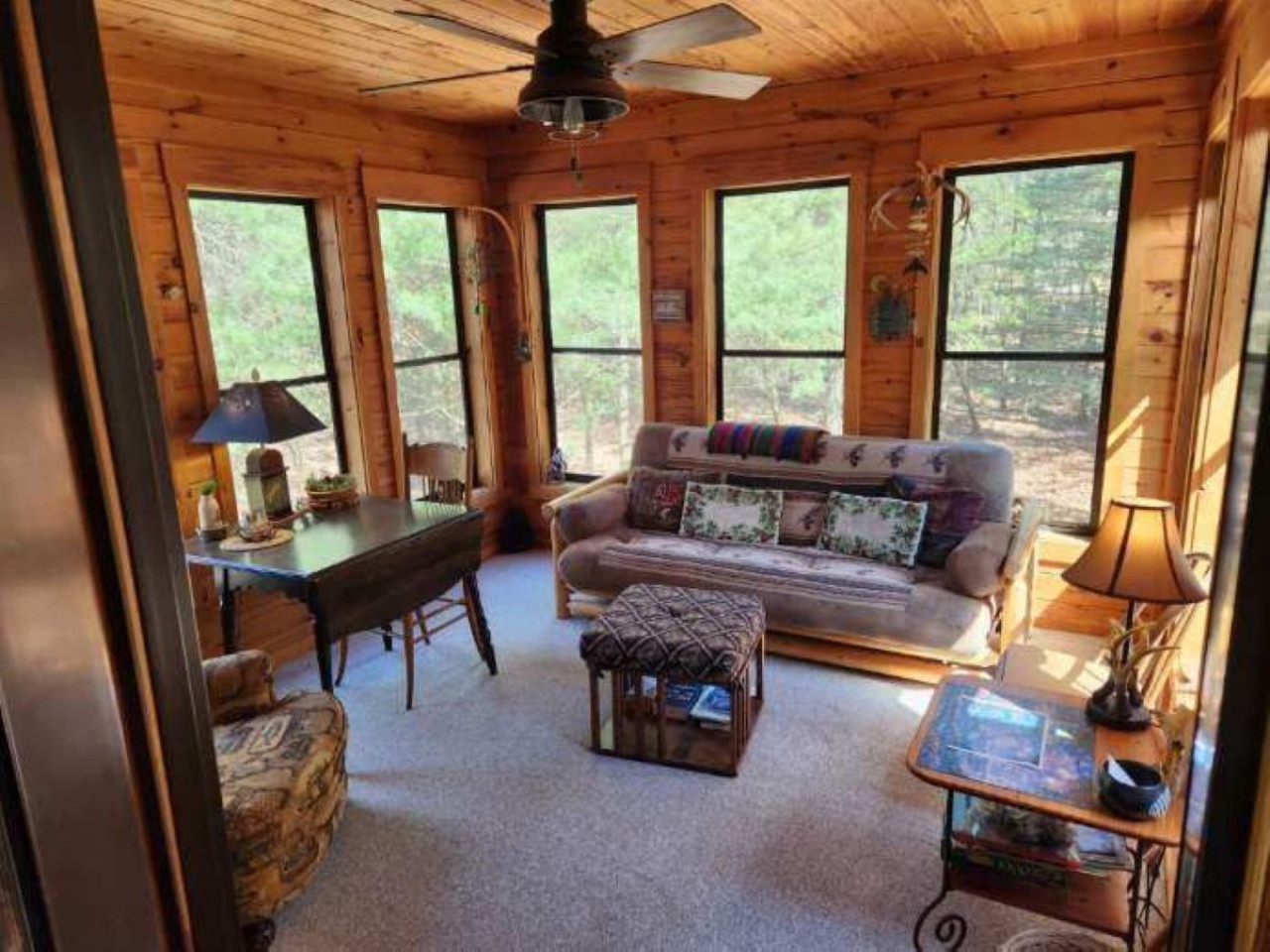 Relax in your cozy log cabin living room surrounded by panoramic windows that frame peaceful forest views.