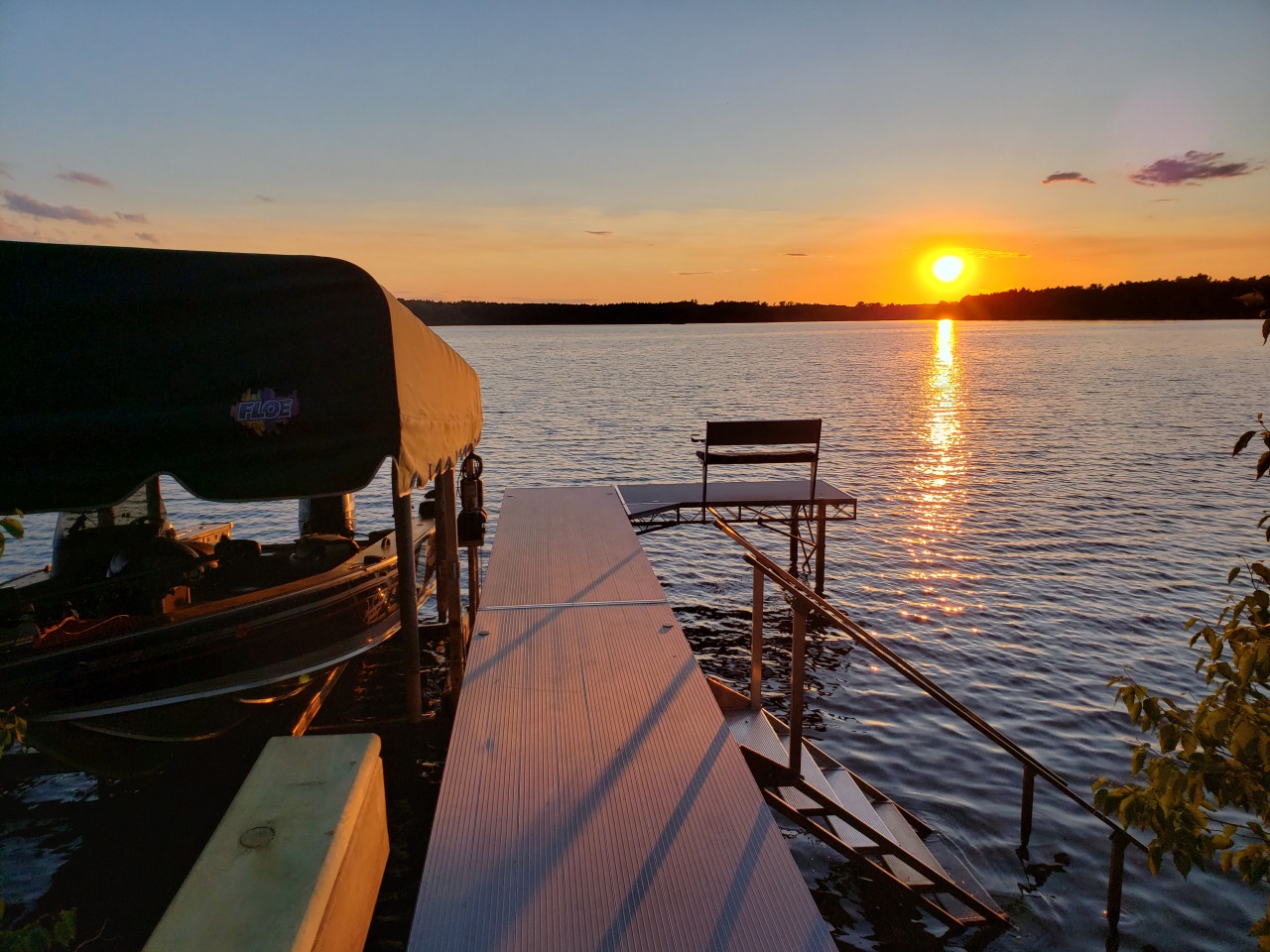 A stunning lakeside dock with boat lift overlooks the water during a golden sunset, offering peaceful waterfront access.