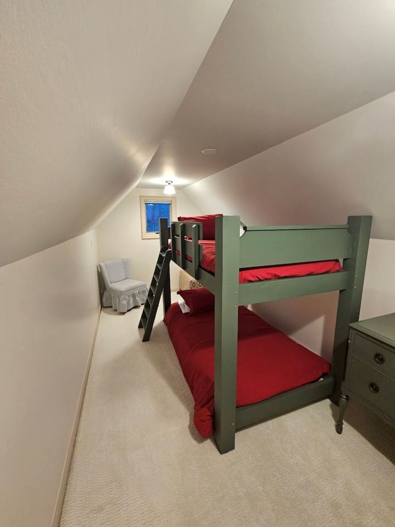 Your cozy attic bedroom features charming green bunk beds with vibrant red linens, perfect for kids or extra guests to rest comfortably.