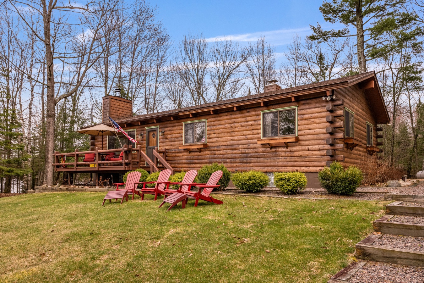 Classic log cabin nestled among towering trees with spacious deck and Adirondack chairs on manicured lawn for peaceful forest retreat.