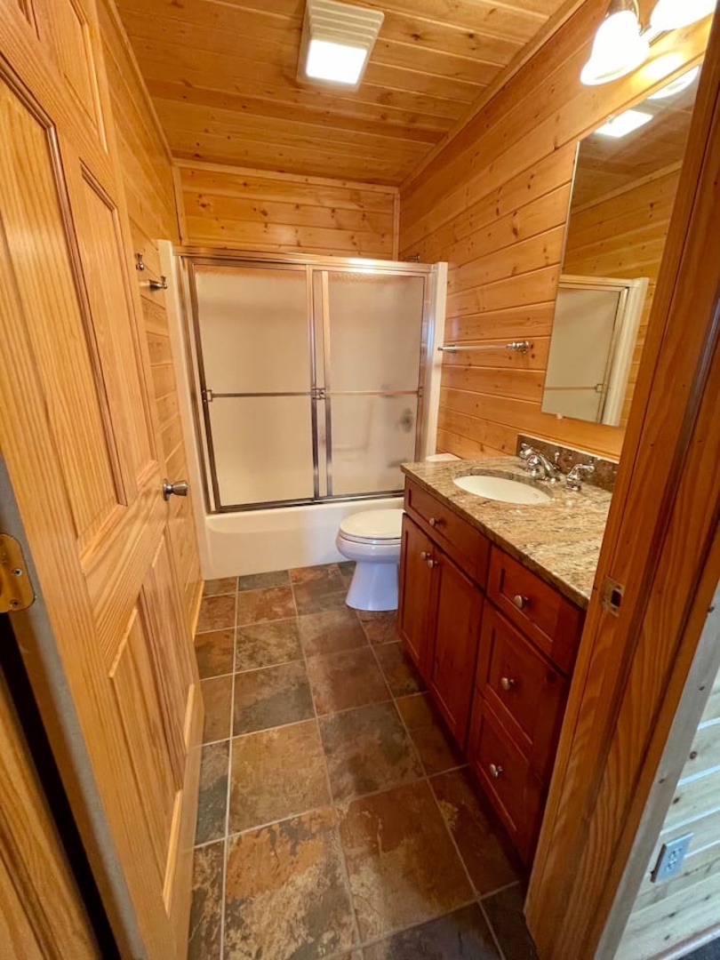 Step into your private retreat—warm wood walls frame a spacious bathroom with granite counters and glass shower doors.