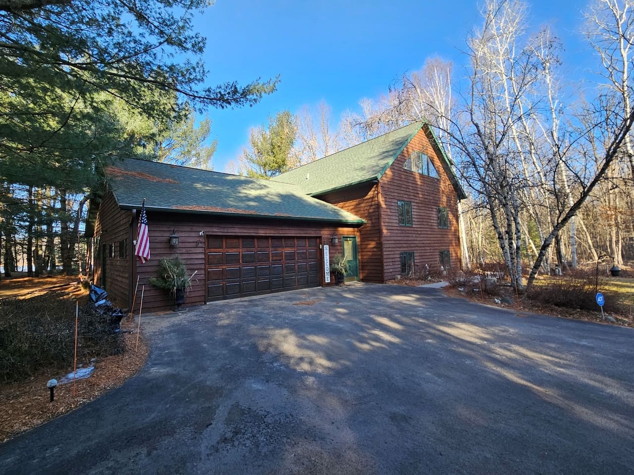 Charming wood-sided cabin nestled among towering trees with convenient driveway parking and welcoming entrance.