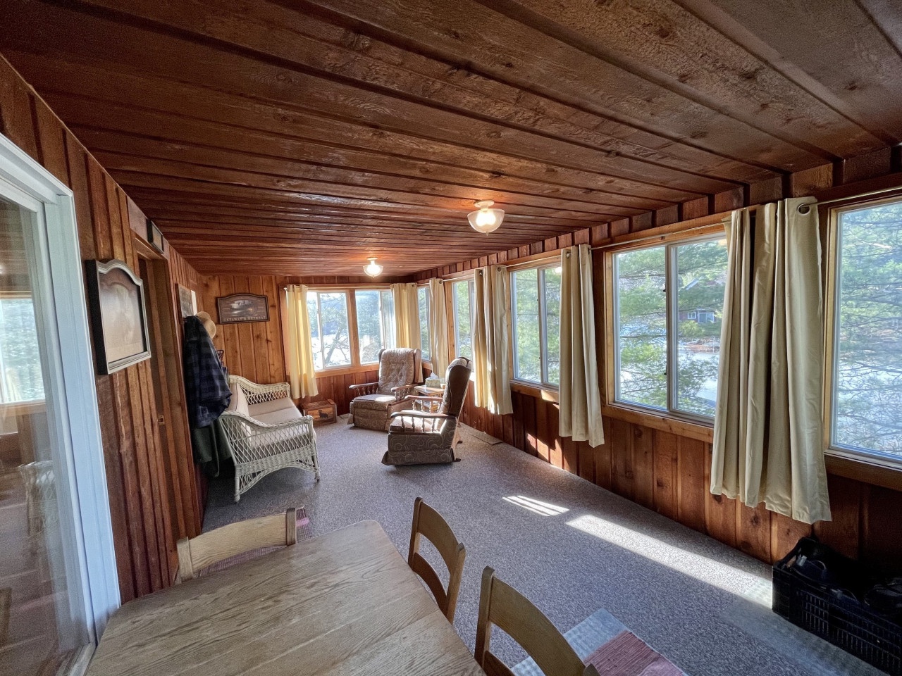 Unwind in your rustic sunroom with warm wood walls and panoramic windows showcasing peaceful lake views.