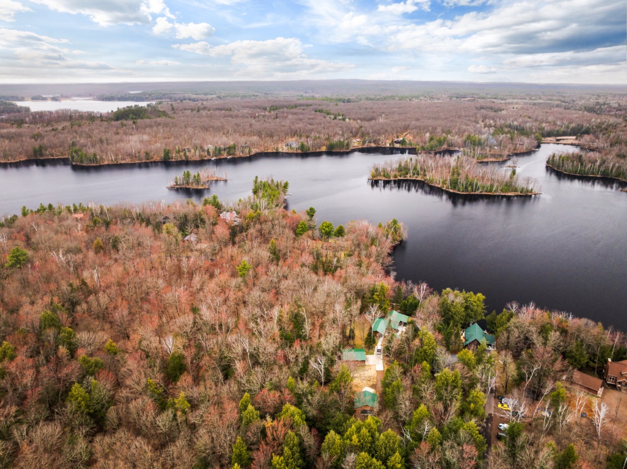 Stunning aerial perspective reveals a lakefront property nestled among fall foliage, with pristine waters and wooded islands creating a peaceful retreat setting.
